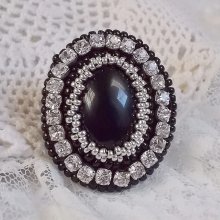 Bague Stone Noire avec un cabochon en Onyx orné de chatons en Cristal à laquelle s’ajoute des rocailles Argentées qui complètent le Noir sur bague Nickel en Laiton et une feutrine. Un style Rétro